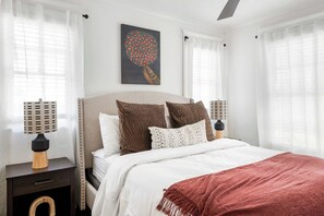 A bedroom with a bed, two nightstands, a wall art piece, and sheer curtains. - Ready Aim (Atlanta)