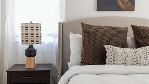 Un lit bien fait, agrémenté d’oreillers à motifs, une table de chevet avec une lampe et une œuvre d’art accrochée au mur.