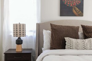 A neatly made bed with patterned pillows, a bedside table with a lamp, and a wall-mounted artwork. - Ready Aim (Atlanta)