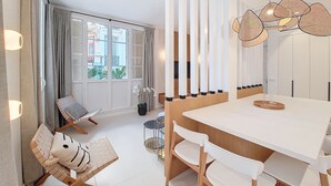 A modern dining area with a white table and chairs, a wicker pendant light, and a view of the outside through large windows with shutters. - N&J - PALMIERS TERRASSE - Central - Terrace (Niza)
