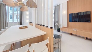 A modern living room with a large TV, a dining area with a white table and chairs, and a decorative light fixture. - N&J - PALMIERS TERRASSE - Central - Terrace (Niza)