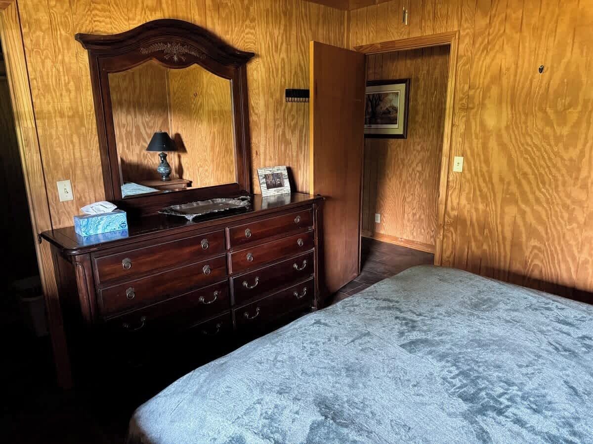 A bedroom with a wooden dresser, a bed, and a mirror.