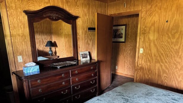 A bedroom with a wooden dresser, a bed, and a mirror.