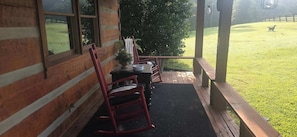 A wooden porch with a table and chairs, a potted plant, and a view of a grassy yard. - Harpeth Moon Summary: (Kingston Springs)