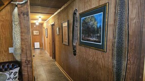 A wooden hallway with framed pictures on the walls, a fur coat on the left, and a patterned rug on the right.