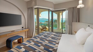 Une chambre d’hôtel moderne dotée d’un grand lit, d’un téléviseur à écran plat fixé au mur, d’un bureau avec une chaise et d’un balcon offrant une vue sur la mer.