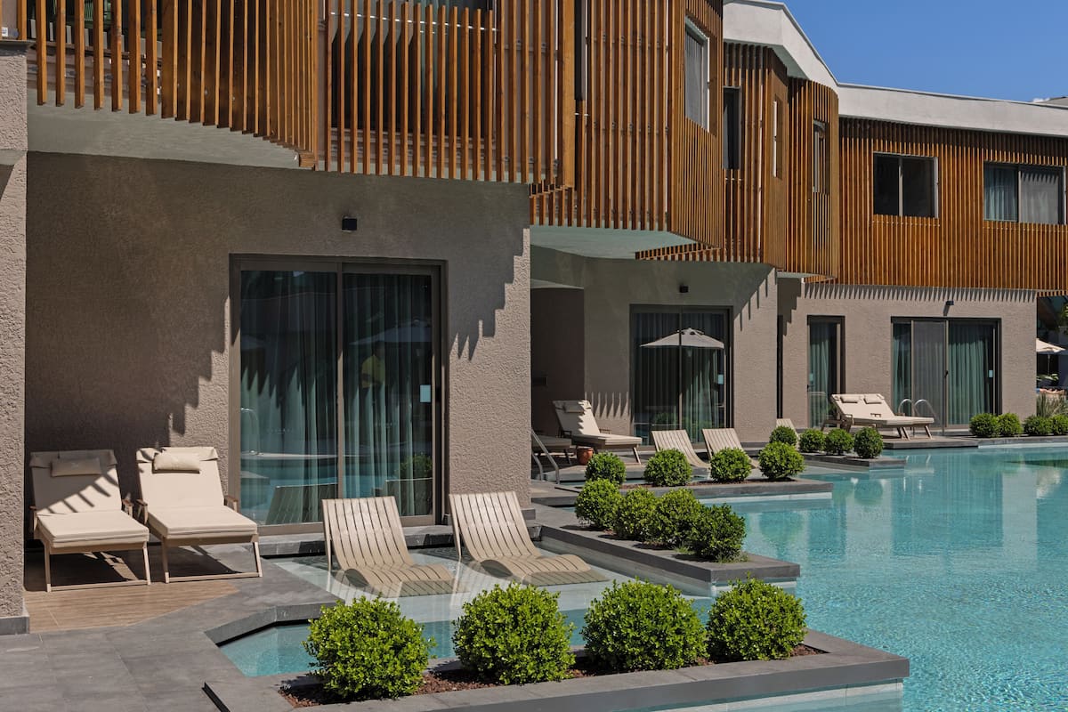 A modern hotel with a swimming pool, lounge chairs, and a wooden deck.