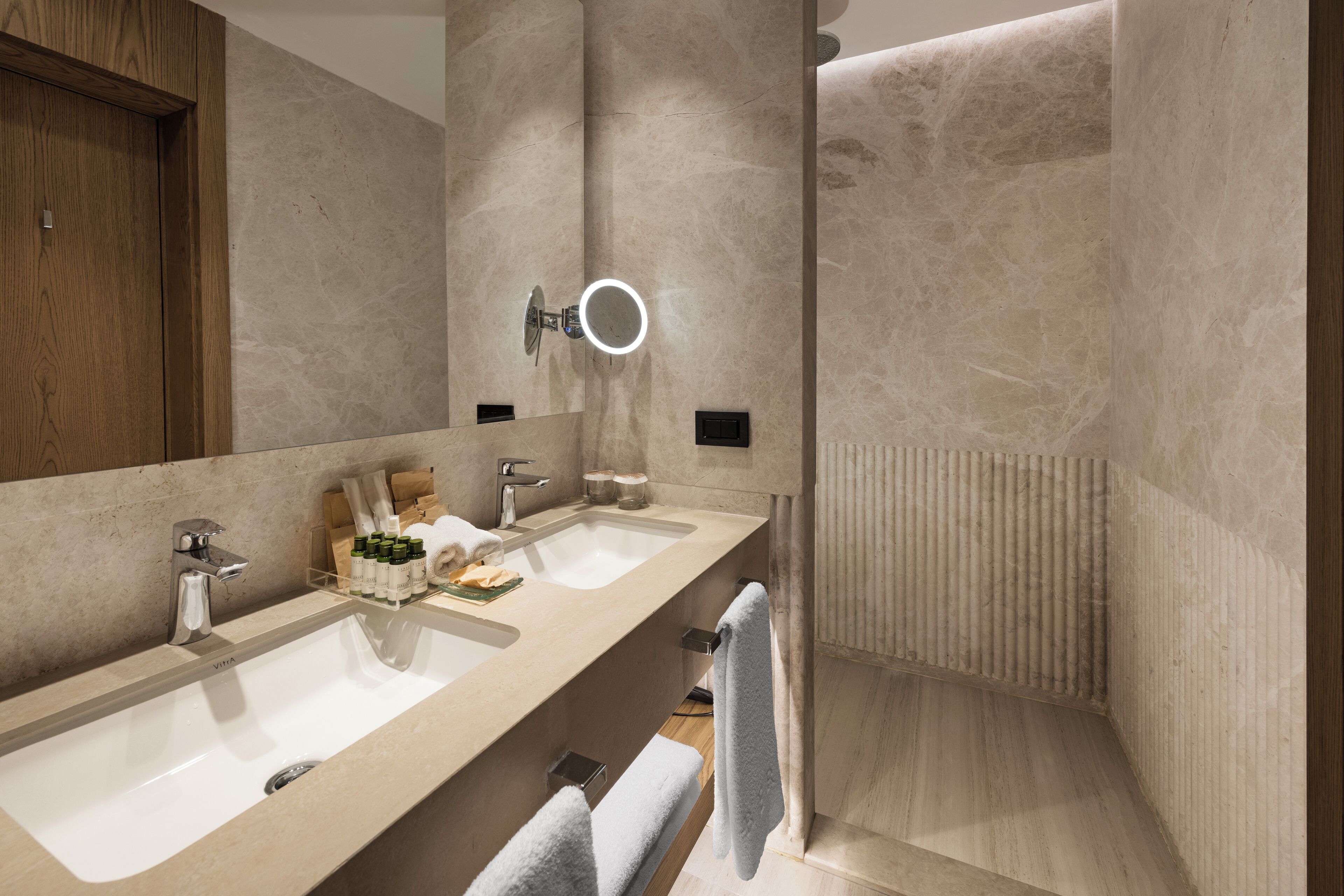 A modern bathroom with two sinks, a mirror with a ring light, and a shower area.