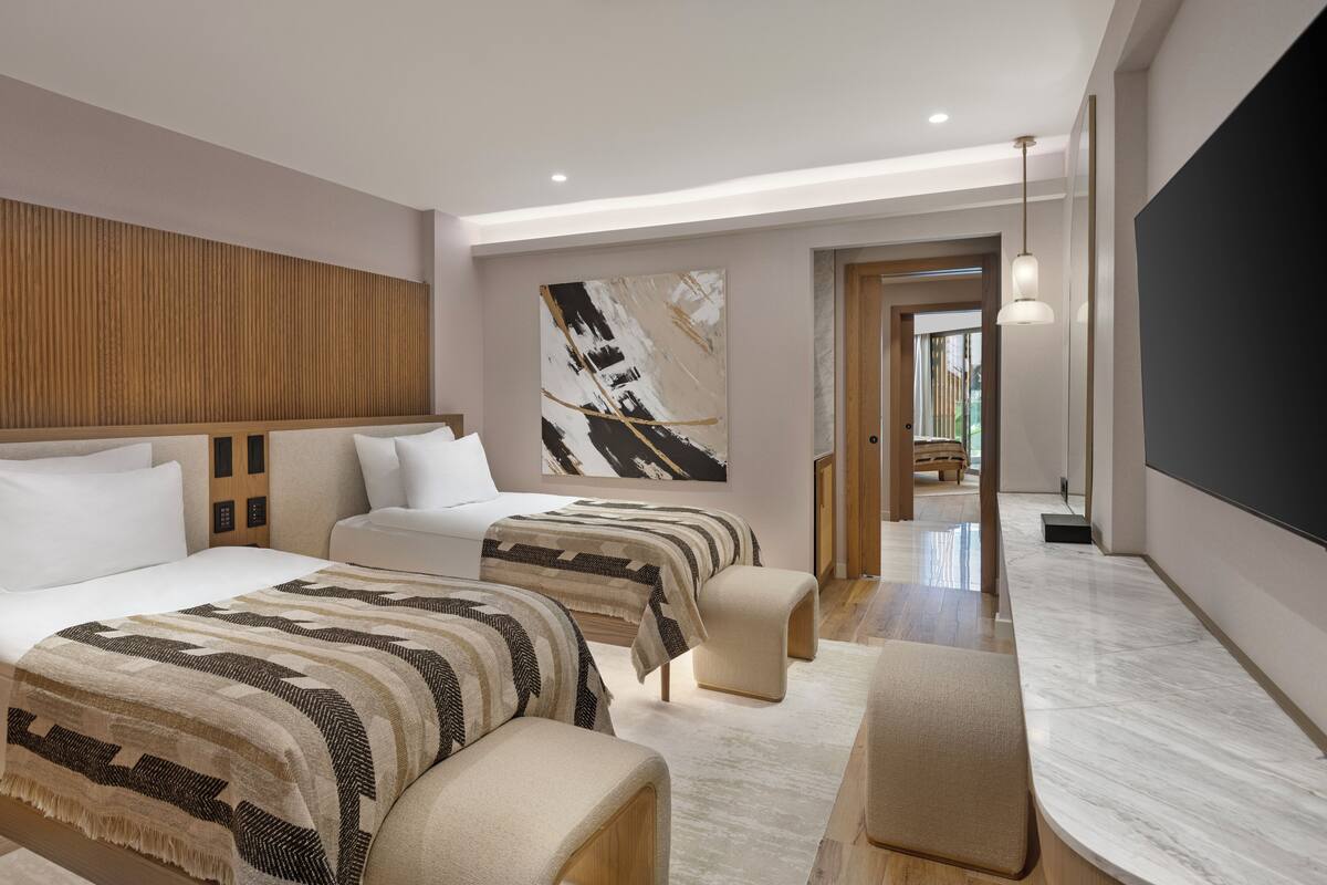 A modern hotel room with two beds, a large abstract painting, a wooden headboard, and a view of the hallway.