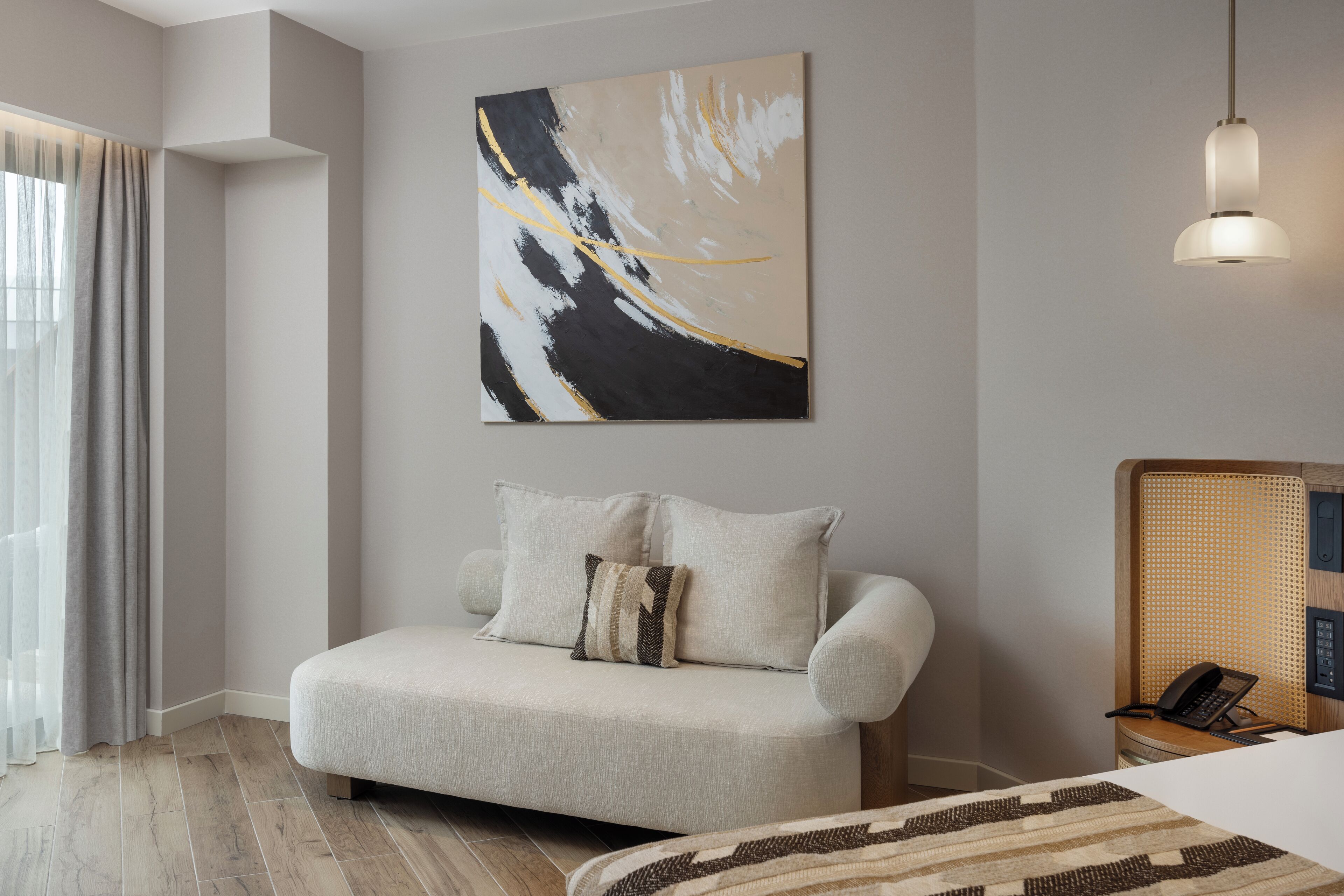 Een moderne hotelkamer met een bank, een schilderij aan de muur, een bed en een telefoon op een bijzettafeltje.