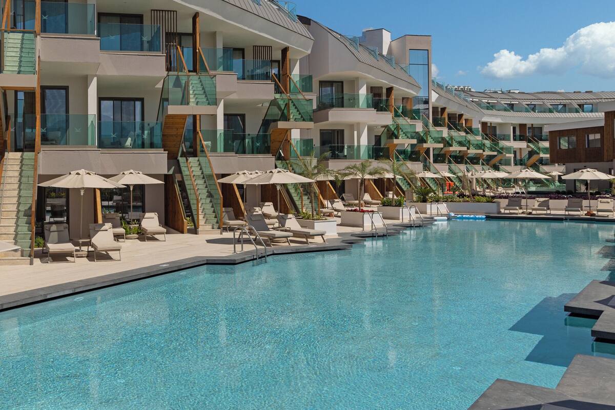 A modern hotel with a pool area, multiple balconies, and sun loungers.