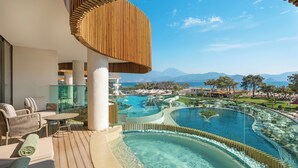 A balcony with wicker furniture, a glass table, and a view of a pool and mountains.