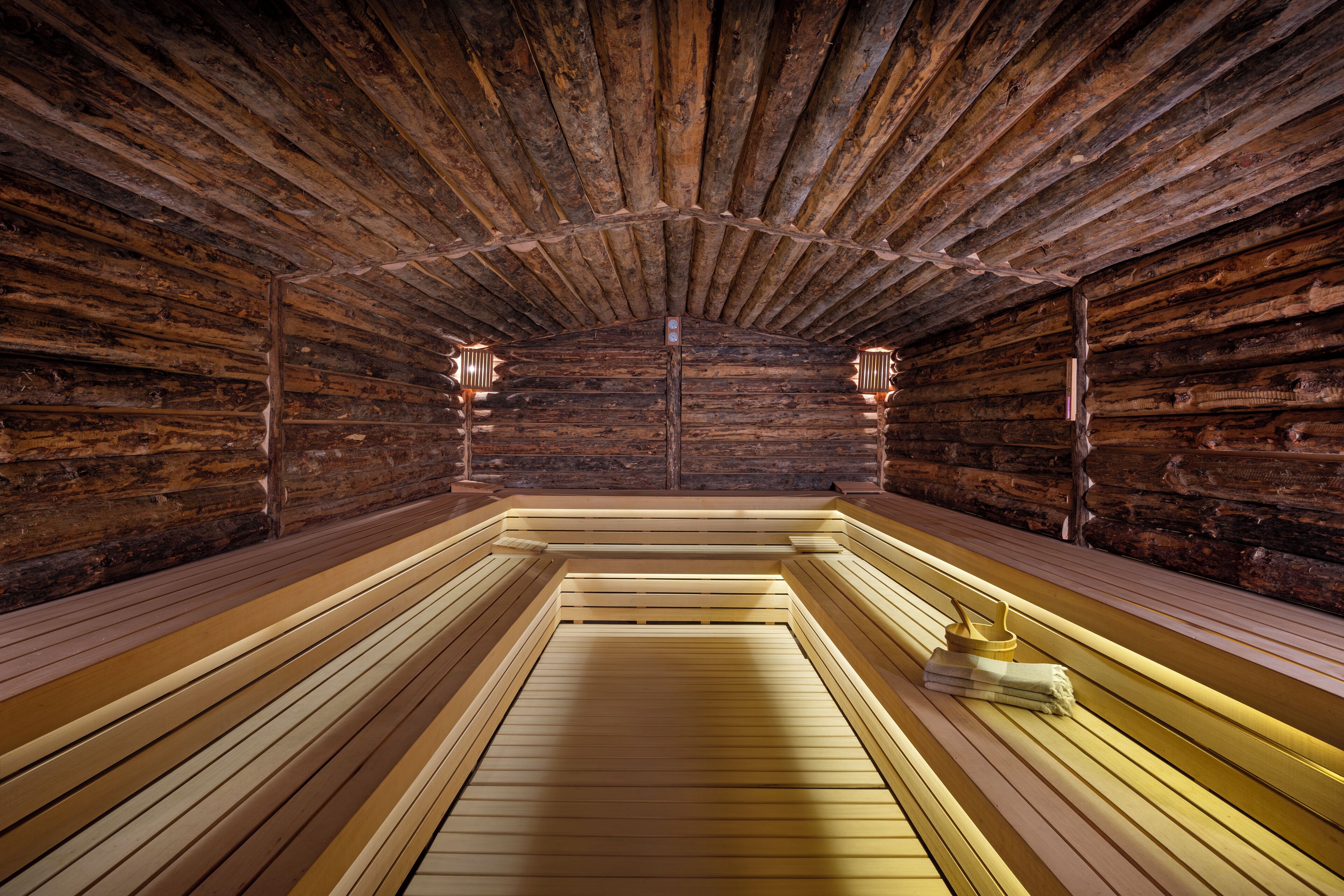 A sauna room with wooden benches and benches, a wooden ceiling, and two wall-mounted lights.
