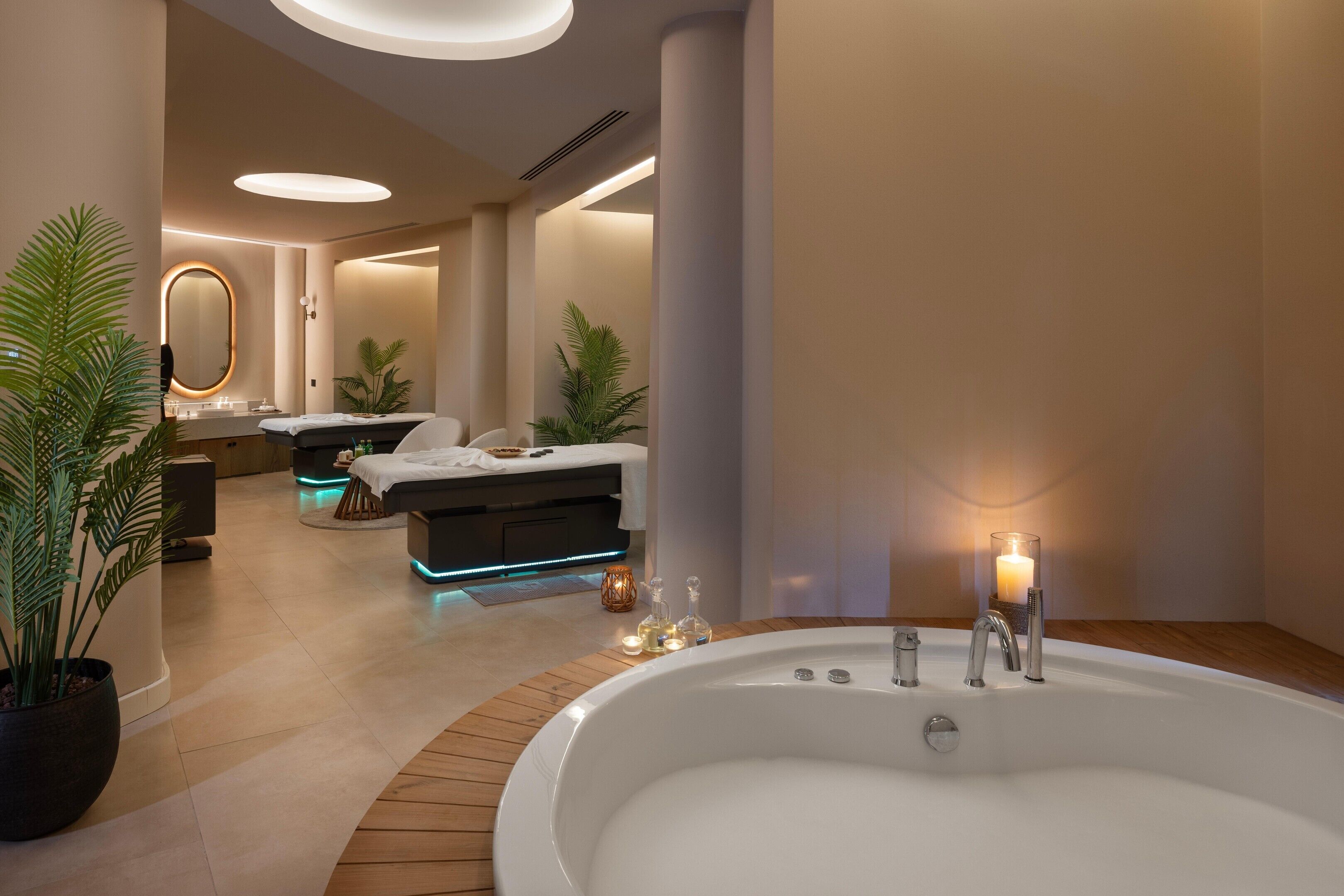 Un moderno cuarto de spa con una bañera grande, una camilla de masaje y una zona de tocador bien iluminada.