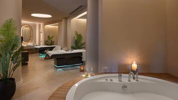 Un moderno cuarto de spa con una bañera grande, una camilla de masaje y una zona de tocador bien iluminada.