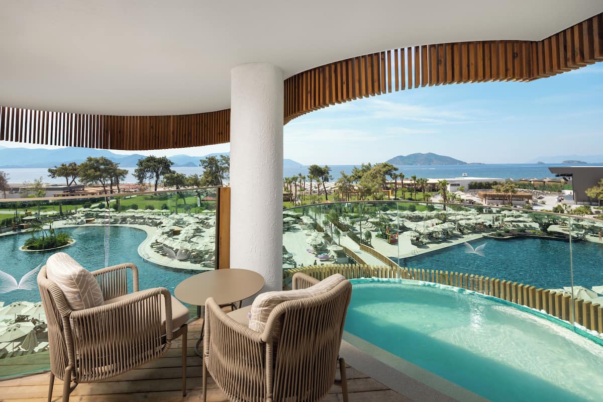 A balcony with wicker chairs and a table overlooking a pool and resort area.