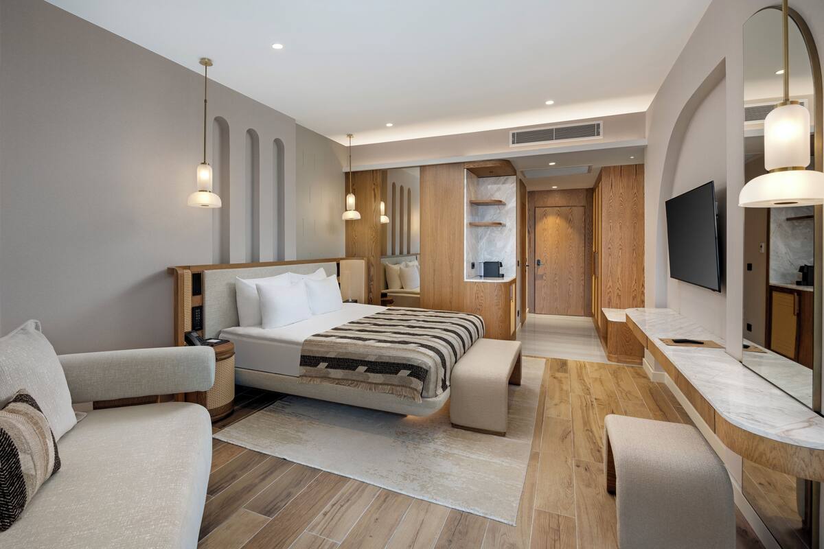 A modern hotel room with a large bed, a sofa, a desk, and a TV.