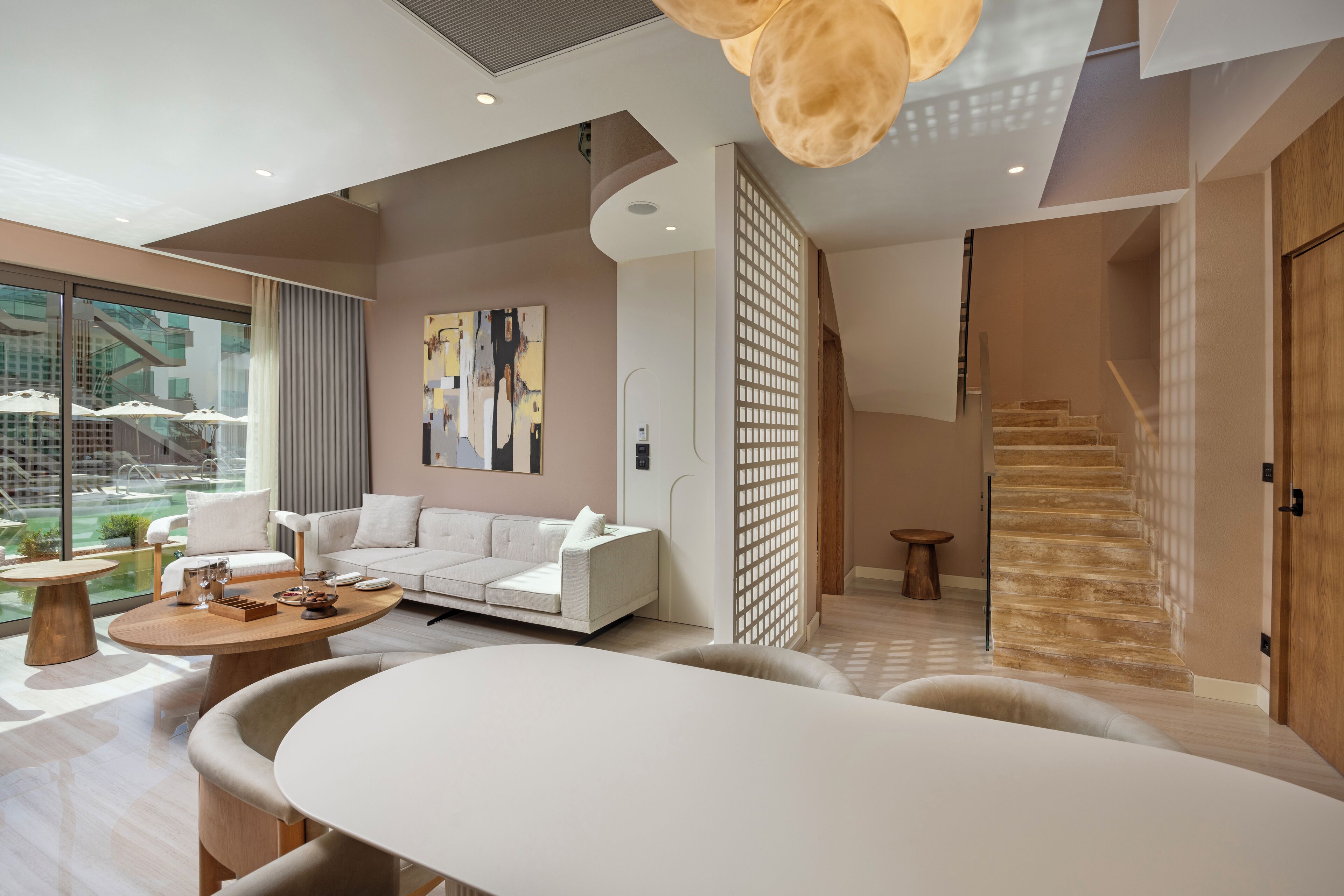 Una sala moderna con un sofá blanco, una mesa de centro redonda y un ventanal con vistas a un patio.