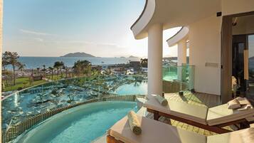 Zona de descanso junto a la piscina con tumbonas, vista a una piscina del resort y una playa y montañas a lo lejos.