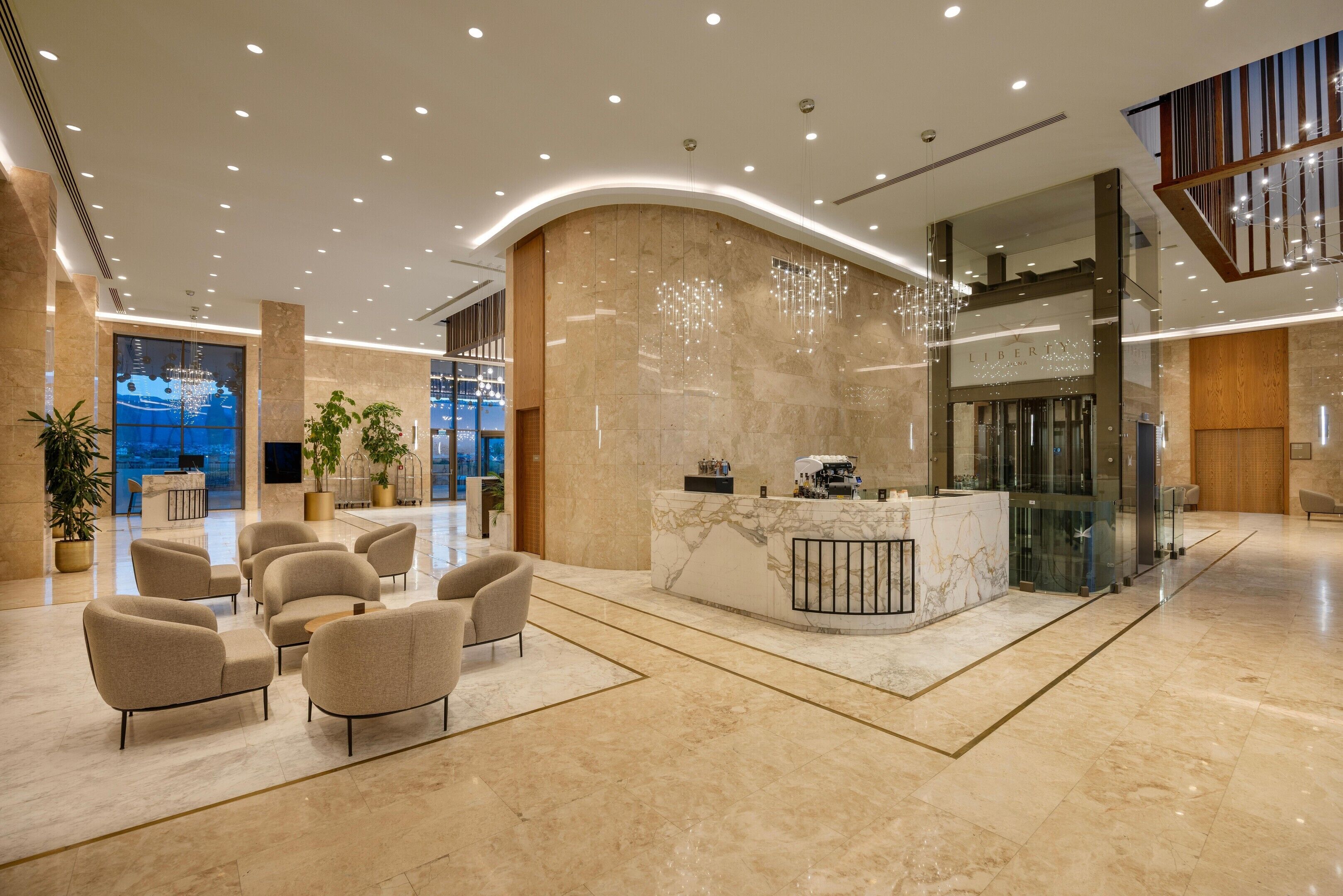 A modern hotel lobby with a reception desk, seating area, and a glass elevator.