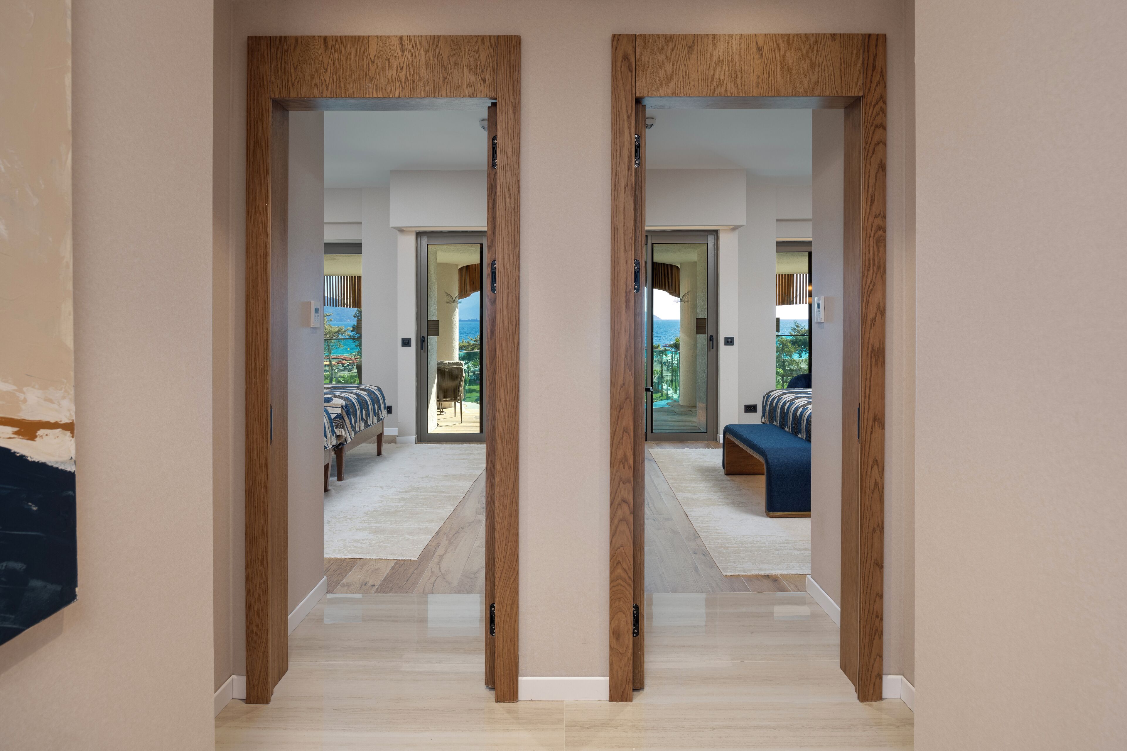 A hallway with wooden doors leading to a room with a bed and a view of the outdoors.