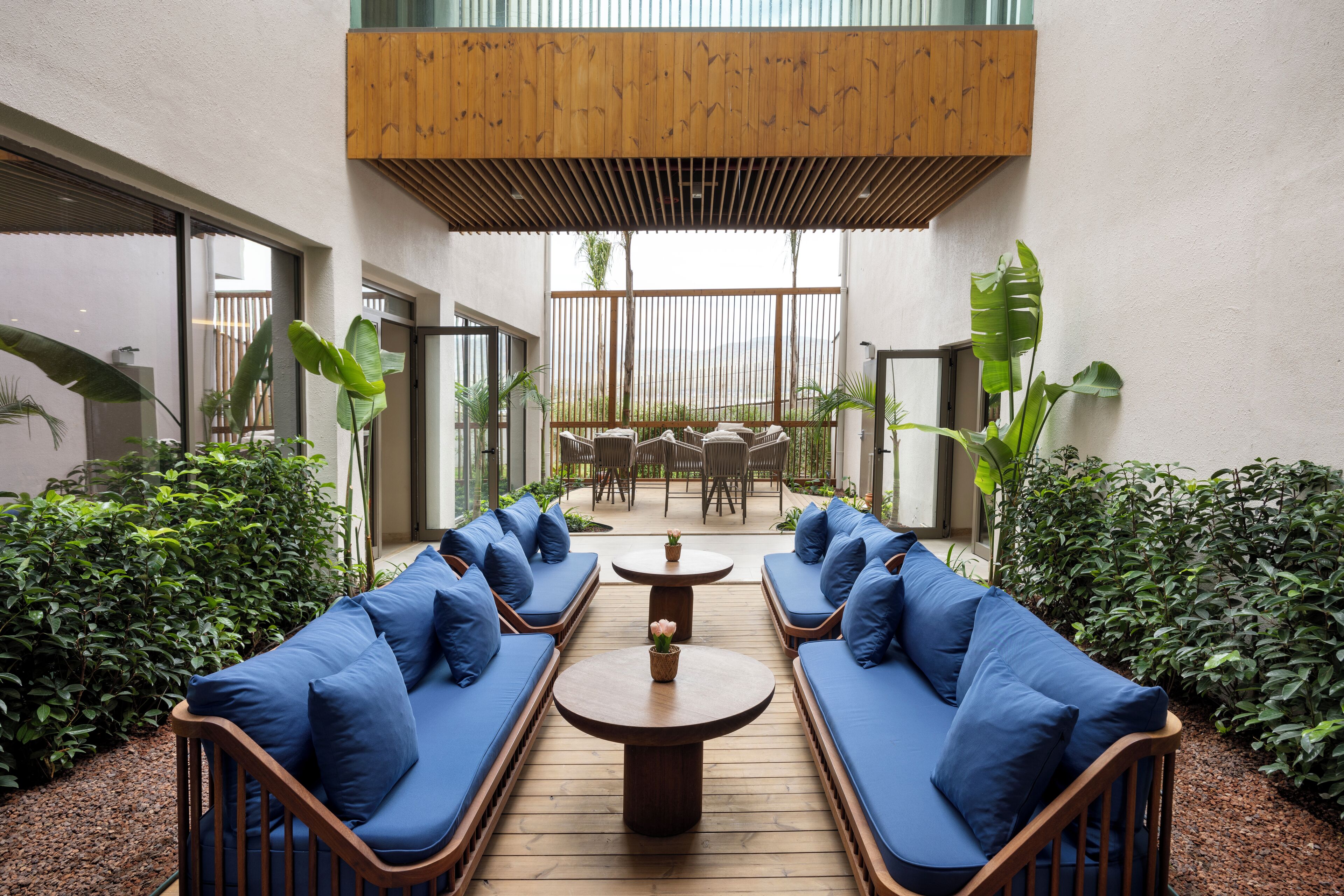 Un espacio de patio con asientos acolchados azules, una mesa de madera y vistas al exterior.