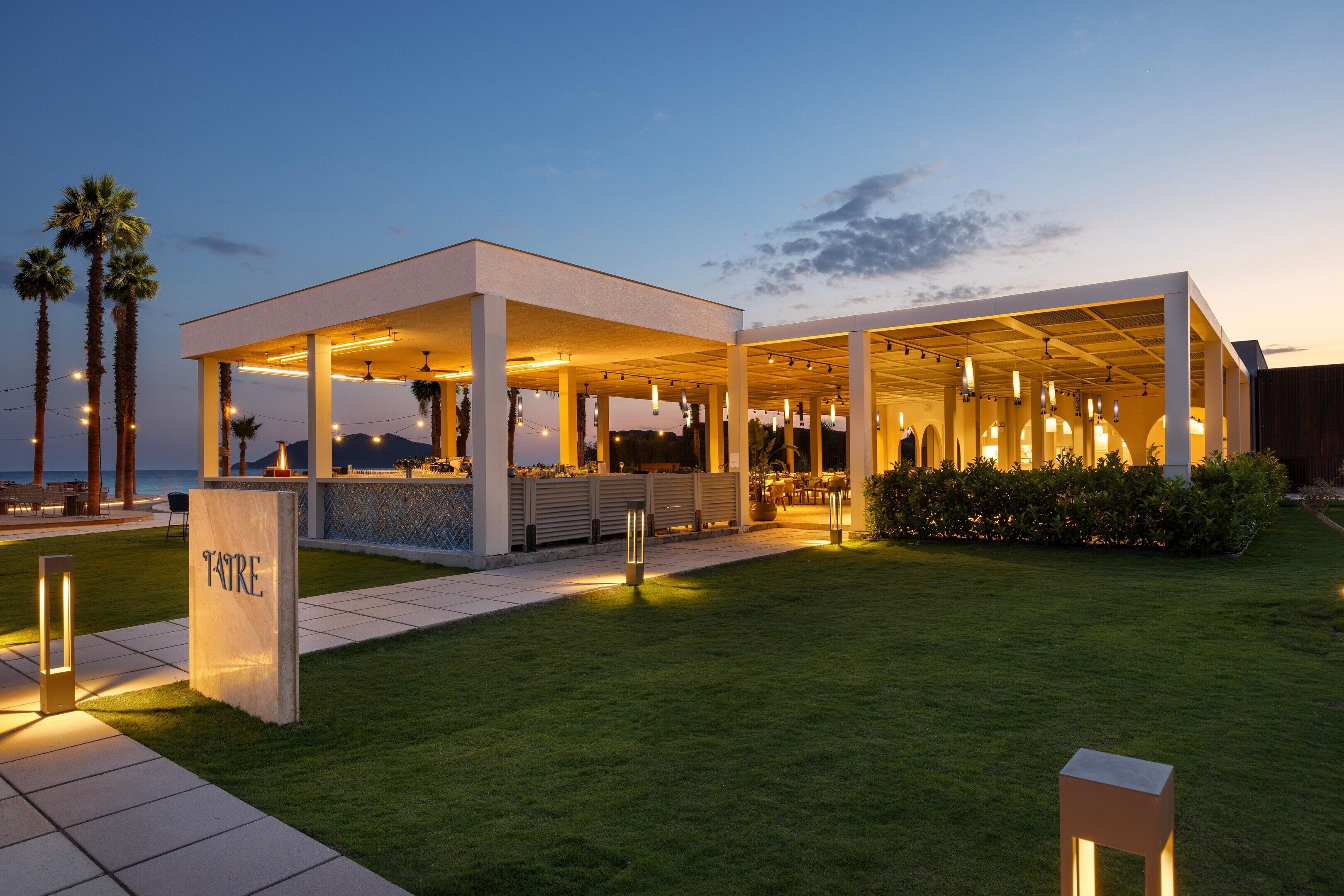 Een modern buitenzitgedeelte met een overdekt terras, een bar en een verzorgd gazon.