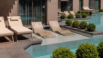 A pool area with lounge chairs and small bushes.