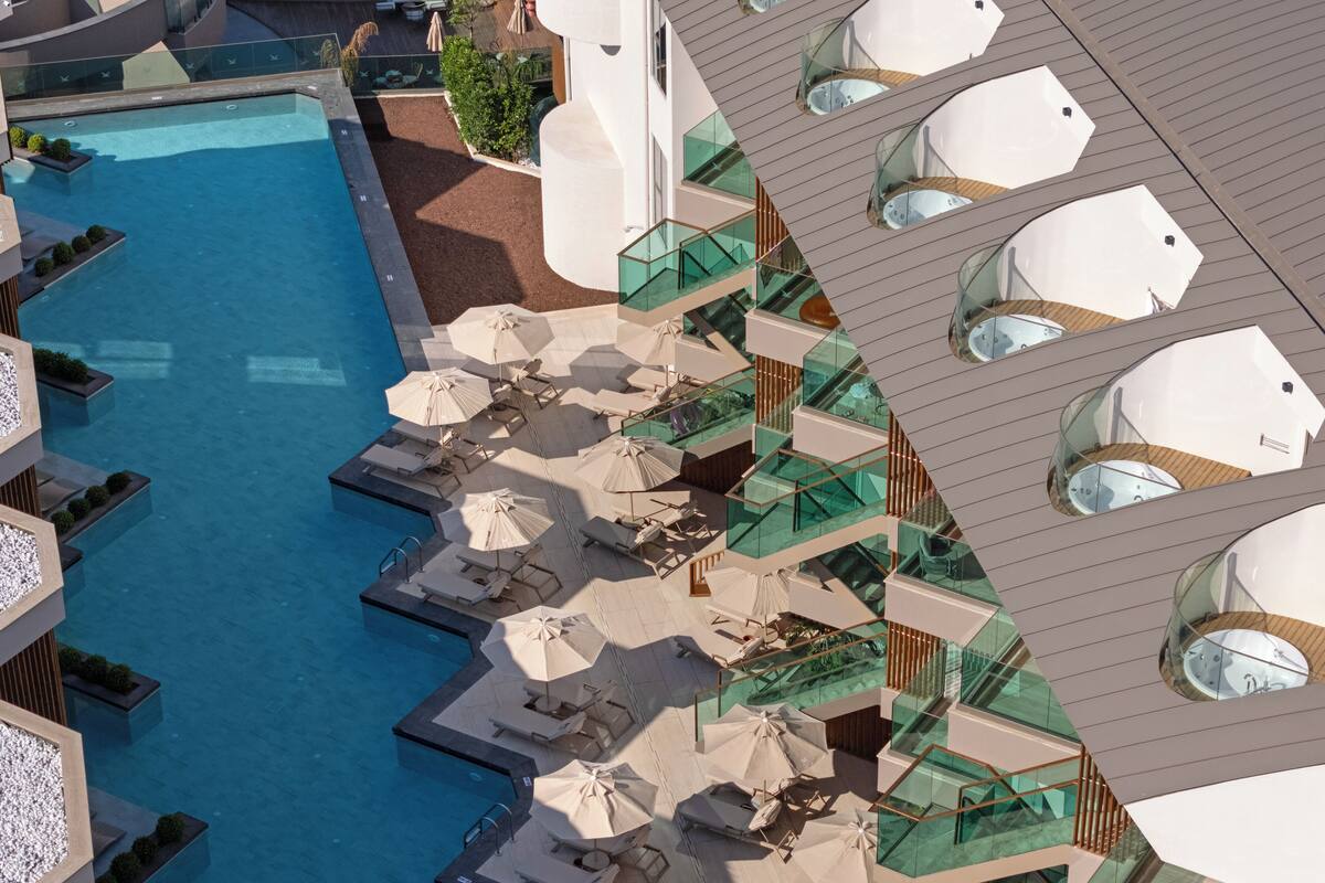 A modern hotel with a large pool, multiple lounge areas with umbrellas, and glass balustrades.