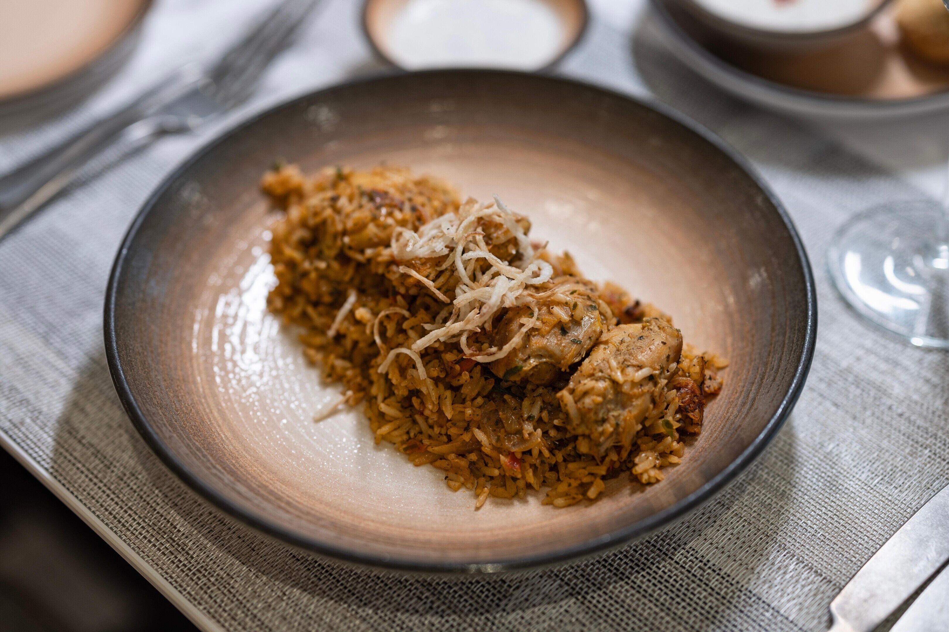 A plate of food with rice and meat, possibly biryani, on a textured tablecloth.