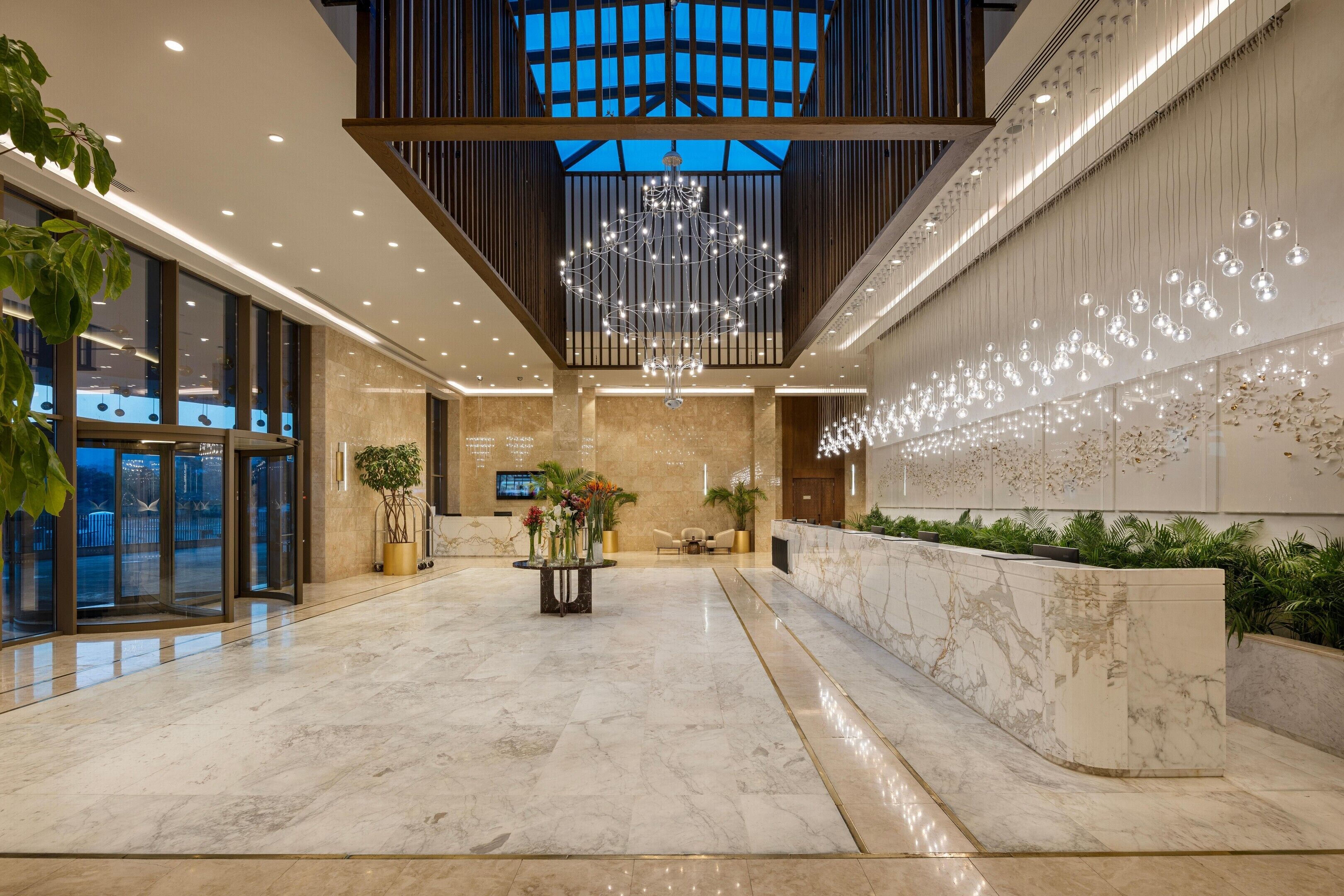 A spacious lobby with a marble floor, a reception desk, and a large chandelier.