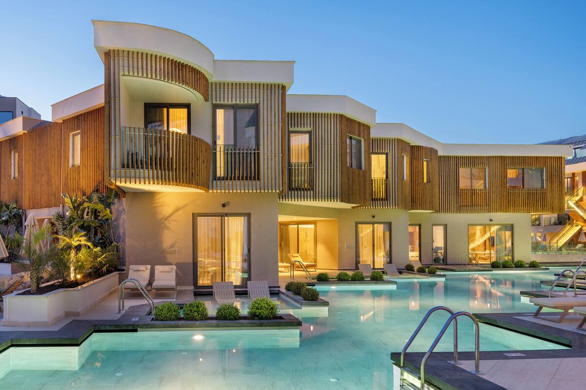 A modern hotel with a pool area, multiple balconies, and a well-lit entrance.
