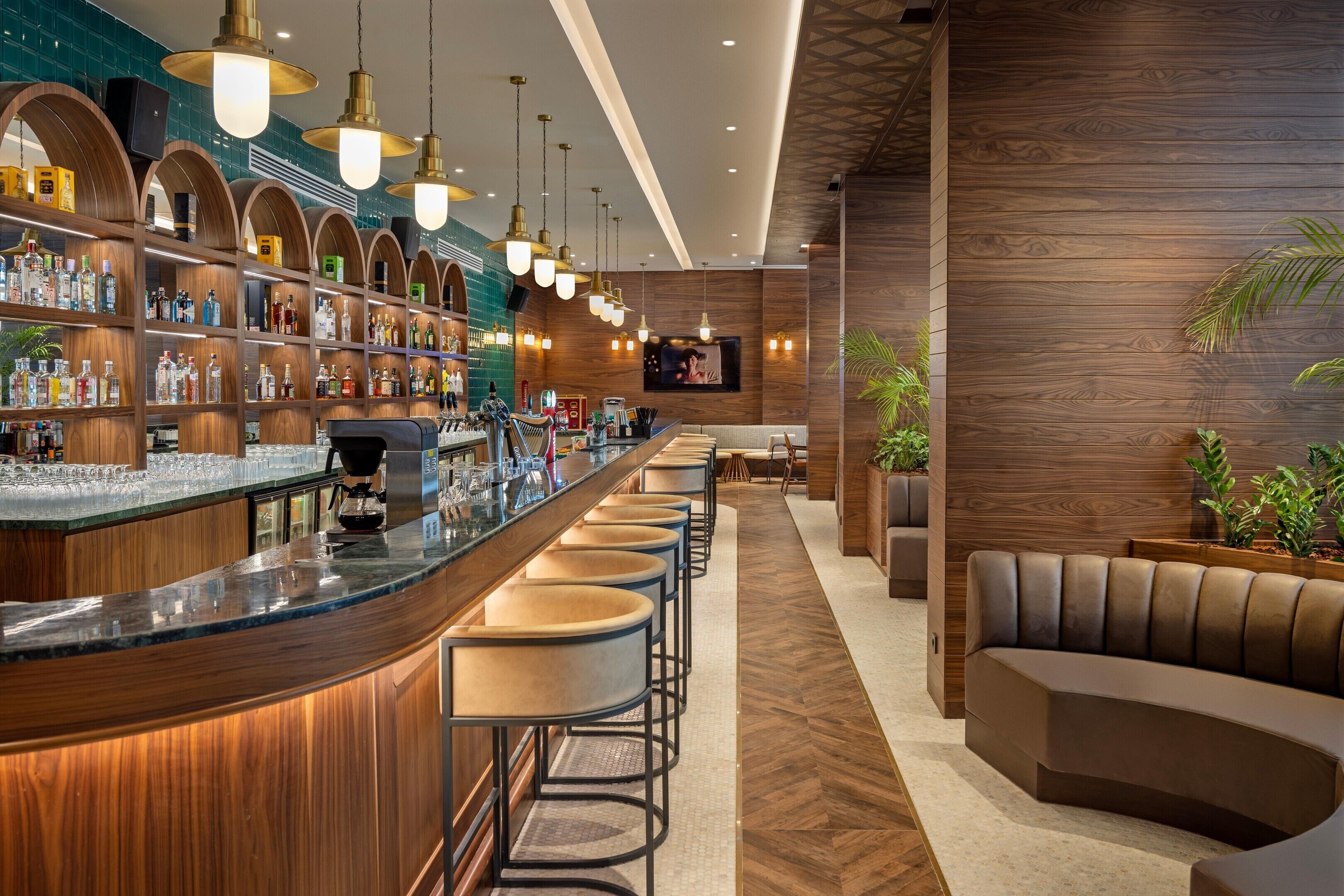 A bar area with a long counter, multiple stools, and a variety of bottles and glasses.