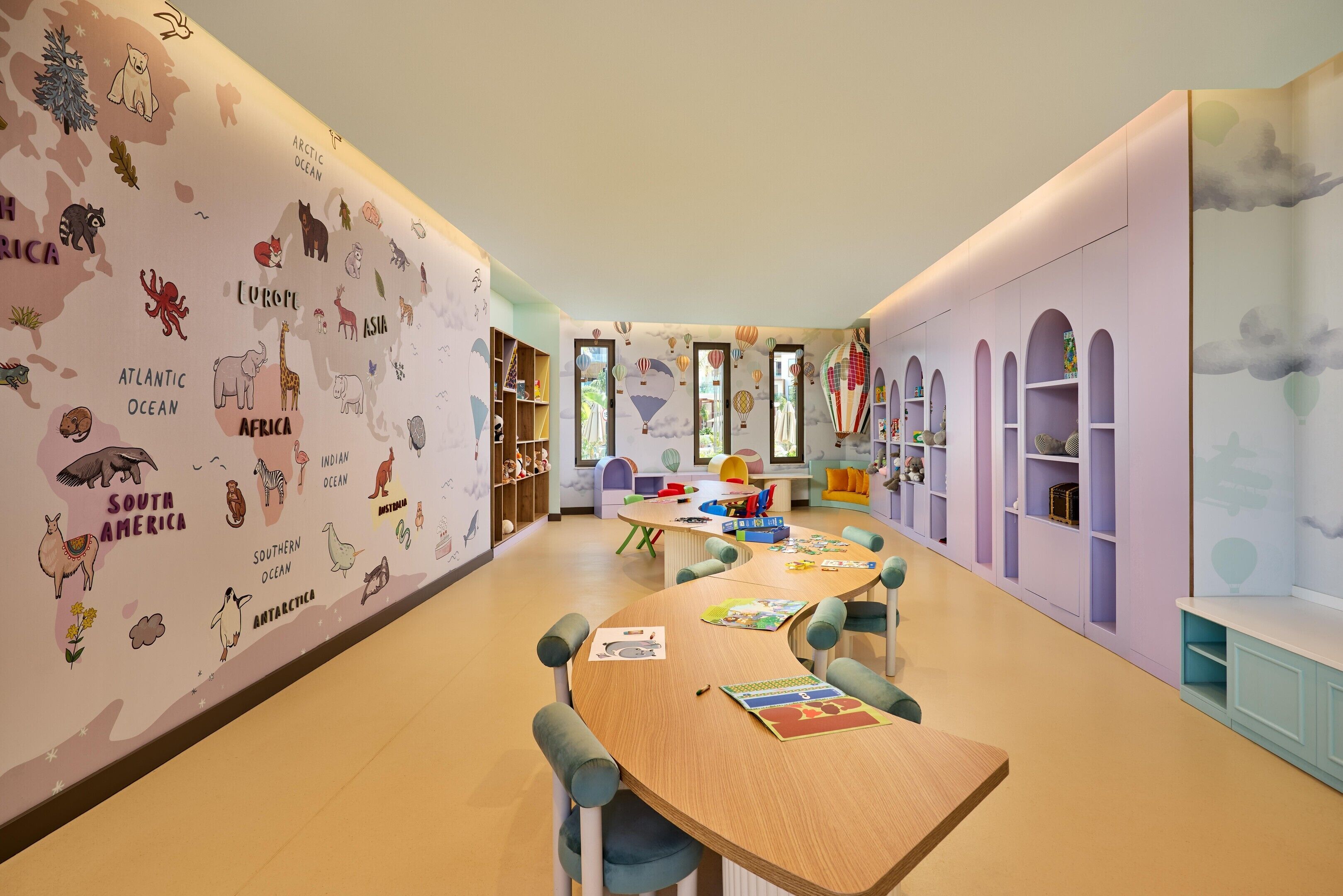 Een kinderspeelruimte met educatieve muurschilderingen, een centrale tafel vol speelgoed en een gezellige zithoek.