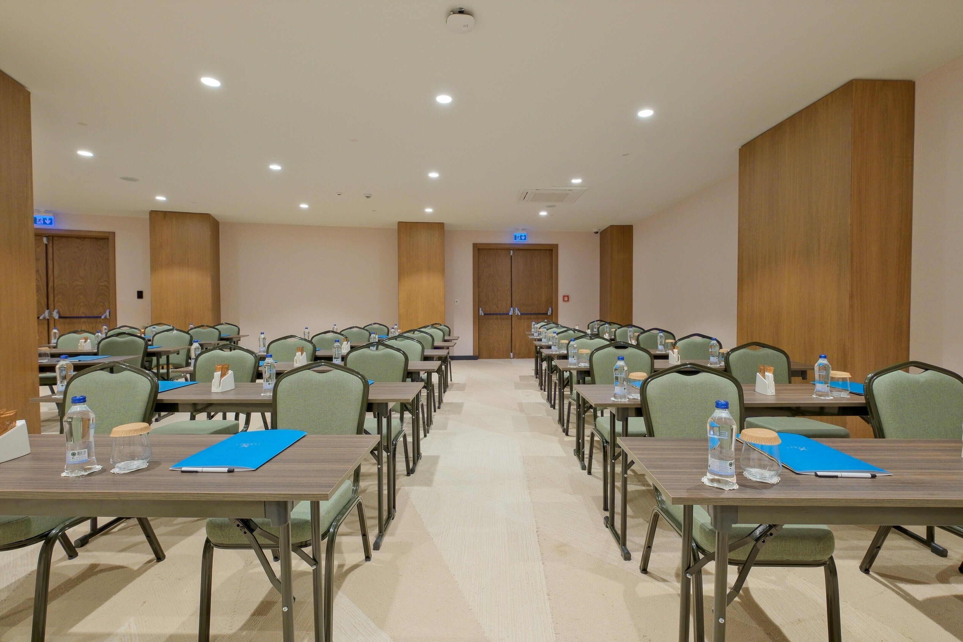A conference room with rows of tables and chairs, equipped with water bottles and folders.