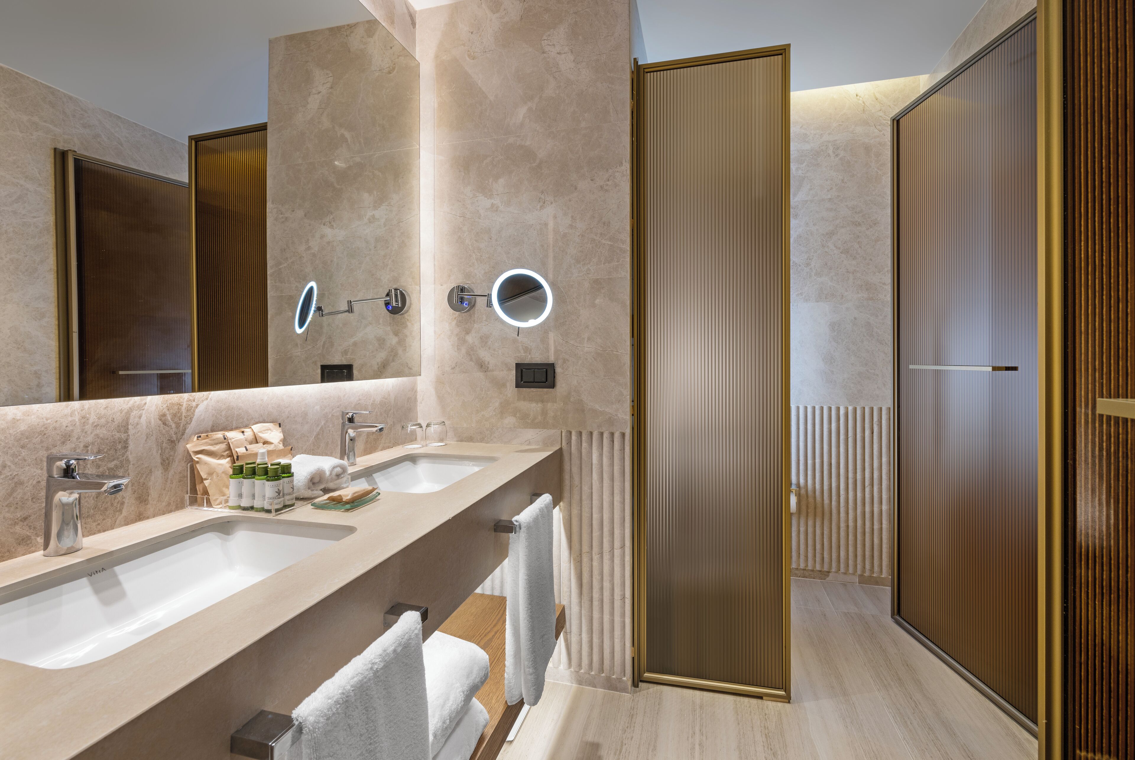 A modern bathroom with two sinks, a large mirror, and a walk-in shower.