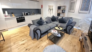 Un salon moderne avec un canapé d’angle gris, une table basse en verre et un plancher en bois.