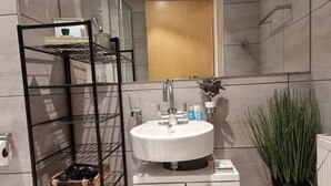 A modern bathroom with a white sink, a black metal shelf unit, and a potted plant. - Large Duplex 7 Adults at London Bridge (London)