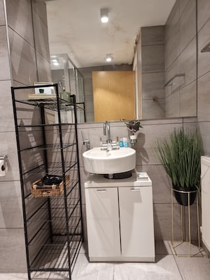 A modern bathroom with a white sink, a black metal shelf unit, and a potted plant. - Large Duplex 7 Adults at London Bridge (London)