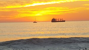 A sunset over a calm sea with a sailboat and a cargo ship in the distance. - Sea Point; Secure 100m² top floor 2 bed apartment with mountain views (Sea Point)
