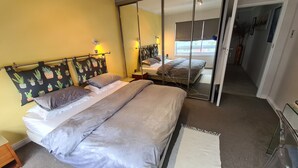 A bedroom with two beds, a mirror, and a view of the hallway. - Sea Point; Secure 100m² top floor 2 bed apartment with mountain views (Sea Point)