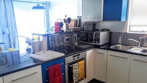 A modern kitchen with a gas stove, microwave, toaster, and a sink. - Sea Point; Secure 100m² top floor 2 bed apartment with mountain views (Sea Point)