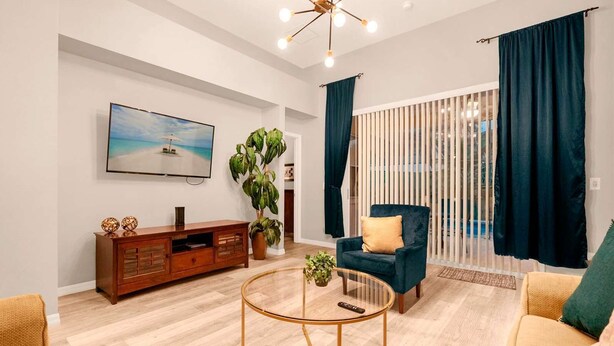 A modern living room with a wooden entertainment unit, a round coffee table, a blue armchair, and a large window with vertical blinds. - Luxe 8-Guest Villa Davenport | Stunning Design (Davenport)