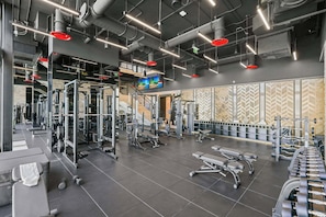 Un gimnasio con equipos de ejercicio variados, una pantalla de televisión y una pared con diseño.