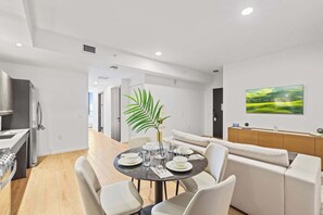 Una cocina moderna con horno empotrado, un comedor con mesa redonda y sillas, y una sala de estar con sofá y un cuadro en la pared.