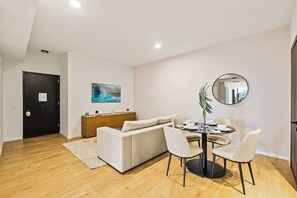 Ein modernes Wohnzimmer mit einer Couch, einem Esstisch, Stühlen, einem runden Spiegel und einem Gemälde an der Wand.