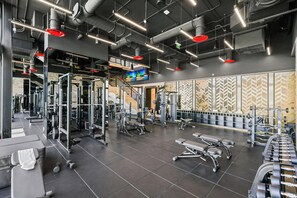 A gym with various weightlifting equipment, a television screen, and a patterned wall. - Bright Resort Style 1BR Heart of Miami Downtown (Miami)