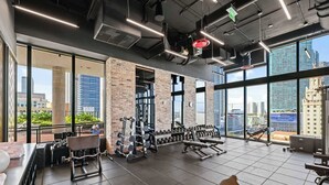 Et fitnesscenter med styrketræningsudstyr, store vinduer og udsigt over bybilledet.