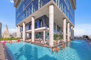 A modern building with a rooftop pool surrounded by lounge chairs and a clear sky.
