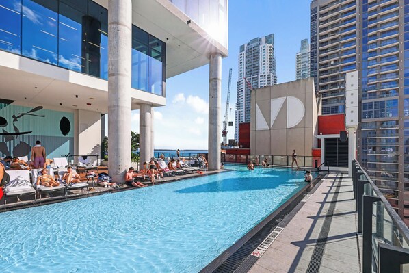 A swimming pool area with lounge chairs and a large building with a distinctive logo.